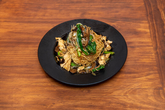 Asian recipe of curly noodles with vegetables and mushrooms sautéed with Korean sauce and bean sprouts on black plate