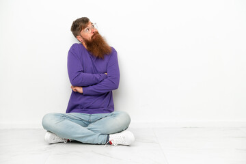 Young caucasian reddish man sitting on the floor isolated on white background making doubts gesture while lifting the shoulders