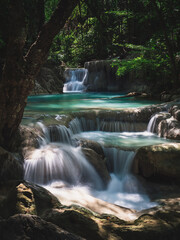 Scenic view of Erawan Waterfall breathtaking peaceful smooth flowing water with sunlight and emerald green pond in lush rainforest. Kanchanaburi, Thailand. Long exposure.