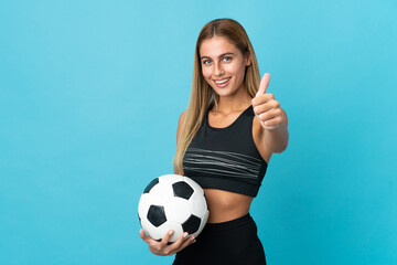 Young blonde woman isolated on blue background with soccer ball and with thumb up