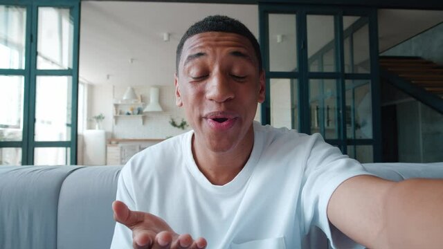 Smiling african american man making selfie or video call while sitting at home on sofa. Portrait of young male blogger doing a video chat from his apartment, while sitting on couch