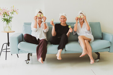 three girlfriends, young women in cosmetic masks, take care of their face on the couch at home and have fun