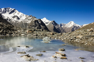 A frozen lake with a view of snow capped Himalayan peaks on a high altitude trek to the Shingo La pass in the Zanskar region in the Indian Himalaya.