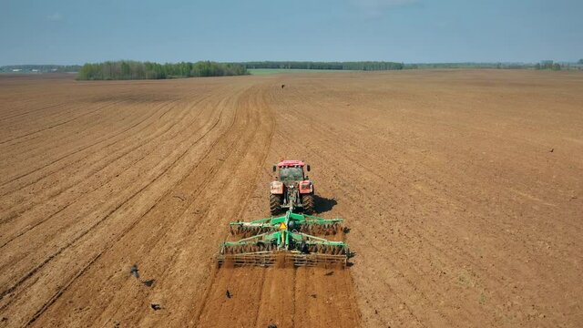 4K Aerial Flat View. Birds In Flock Following For Tractor That Plowing Field In Spring Season. Beginning Of Agricultural Spring Season. Cultivator Pulled By A Tractor In Countryside Rural Field