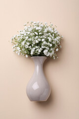 Bouquet of white gypsophila in ceramic vase on beige background, top view