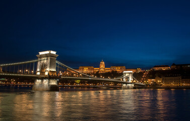 Night view of the old irradiated Chain Bridge in Budapest (Hungary), reflected in the river Danube. In the background you can see the historic houses of the city.