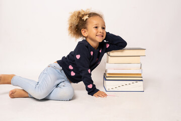 Beautiful little girl in casual clothing with books sitting on the floor isolated over white background.