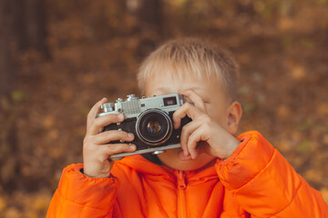 Boy with retro camera taking pictures outdoor in autumn nature. Leisure and photographers concept