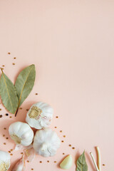 Garlic on pink background with spices, peppercorns and bay leaves. Spices and condiments. Food background. Copy space. Selective focus. 
