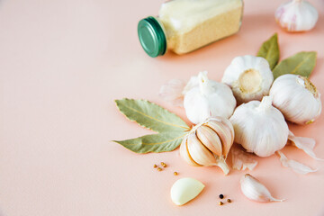 
Garlic bulbs on a pink background with spices, dried garlic, pepper and bay leaf. Spices and condiments. Food background. Copy space.