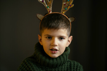 A cute boy in a green sweater and antlers makes a face