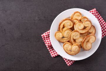 Palmier puff pastry in plate on black background. Top view. Copy space