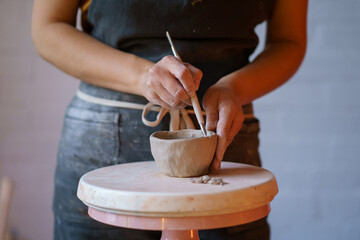 Cropped image of potter in apron shaping vase of raw clay use professional tools and pottery wheel. Ceramist artist female work in studio. Craft ceramics production small business and entrepreneurship