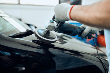 Close-up of worker polishes car hood while working at service workshop.