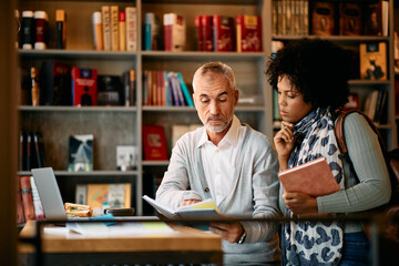 Adult students read lecture notes while learning in library together.