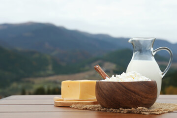 Tasty cottage cheese and other fresh dairy products on wooden table in mountains. Space for text