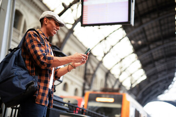 Happy young man waiting for the train. African man waiting in a subway. Man using a phone.