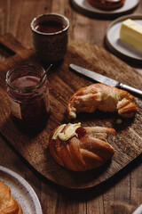 Freshly baked cardamom knot buns (also sweet rolls or swirl buns) with cocoa mug and butter and jam on wooden table. Cosy winter breakfast. Selective focus