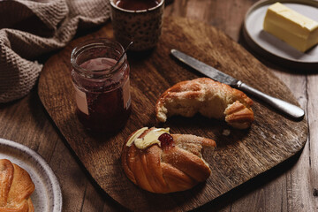 Freshly baked cardamom knot buns (also sweet rolls or swirl buns) with cocoa mug and butter and jam on wooden table. Cosy winter breakfast. Selective focus