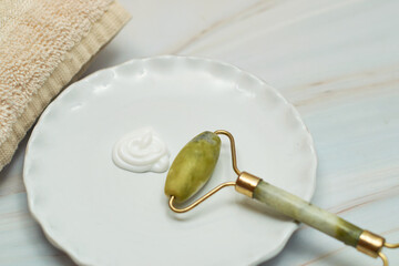 Green jade roller and gua sha stone for facial massage on marble background.