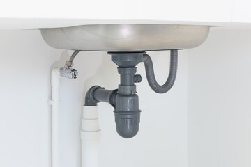 Drain pipe or sewer under kitchen sink. Pvc plastic pipe and
 flexible supply tube connection to stainless steel sink include faucet, trap for drain water and waste in drainage and plumbing system.