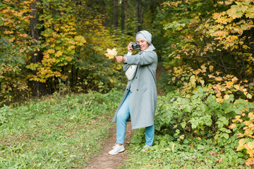 Young Arab Woman wearing hijab headscarf photographing with a smartphone in park. Modern muslim girl
