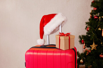 A red suitcase, a Santa Claus hat and a gift box. The concept of traveling for Christmas. Copy space. 
