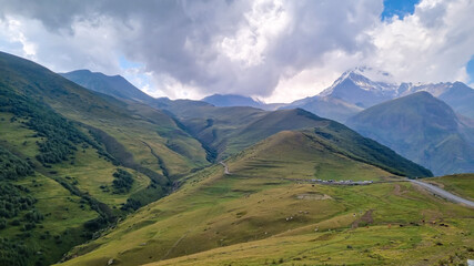 A strong overcast building up above Mount Kazbeg in Caucasus, Georgia. Rainy clouds. There slopes are barren and stony below the snow-capped peak and the Gergeti Glacier. Massive glacier foot