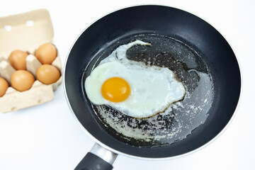 Fry eggs in an old pan and there are a number of eggs in a box on a white background.