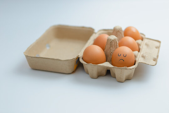 Brown eggs arranged in a box with a sad, lonely face.