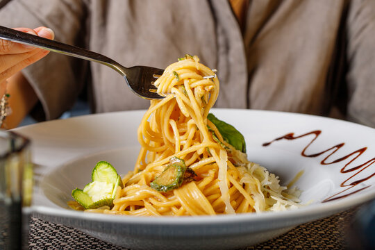 Spaghetti alla nerano con zucchine fritte e provolone del monaco mentre vengono arrotolati con la forchetta
