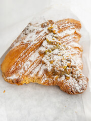 A twice-baked pistachio croissant with powdered sugar in a white bag