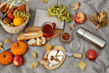 Fototapeta na wymiar Blanket with picnic basket, snacks and autumn leaves, flat lay