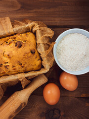 Cake in baking mold with rolling pin on rural rustic wooden background flat lay. Pastry dough recipe ingredients with egg wholegrain flour dried fruits butter sugar vintage wood kitchen table top view