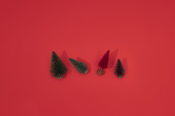 Mini artificial Christmas trees, bottle brush trees for winter decor of green and red color on a red paper background. DIY New Year ornament.