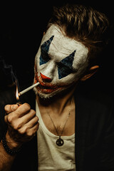 A young man with makeup on his face shows different emotions. Smokes a cigarette, smoke is visible. Black background