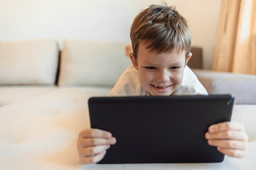 Cropped shot of an adorable little boy using a tablet on the sofa at home. Boy playing with digital tablet. Little boy with digital tablet sitting on sofa, on home interior background.