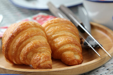 Two croissants on wooden plate.