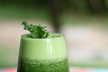 The vegetable green smoothie decorated by kale leaves in a clear glass.