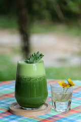 The vegetable green smoothie decorated by kale leaves in a clear glass.