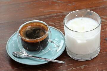 The iced milk and hot coffee in clear glass on the wooden table.
