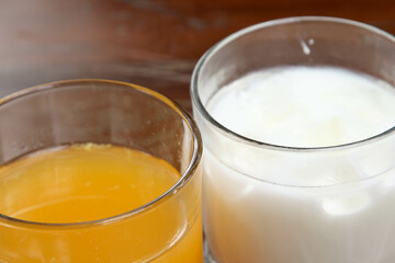 The iced milk and iced orange juice in clear glass on the wooden table.