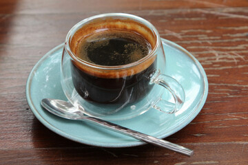 The hot coffee in a clear glass on the wooden table.