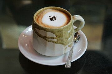 The hot coffee in a ceramic cup on the  table.