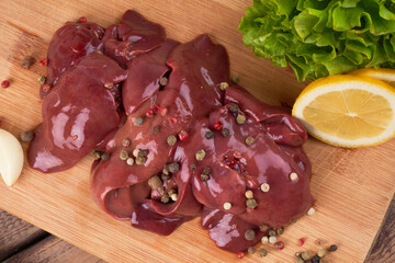 Raw chicken liver on a wooden board, beautifully served with pepper, lemon and herbs