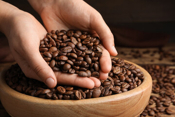 Woman taking pile of roasted coffee beans from bowl, closeup
