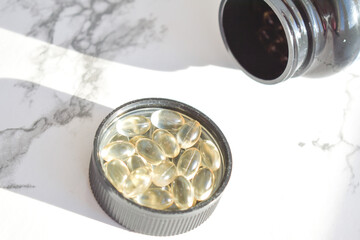 Fish oil capsules with omega-3 and vitamin D in a jar on a white concrete surface
