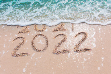 Message Year 2021 replaced by 2022 written on beach sand background. 
Good bye 2021 hello to 2022 happy New Year coming concept.
