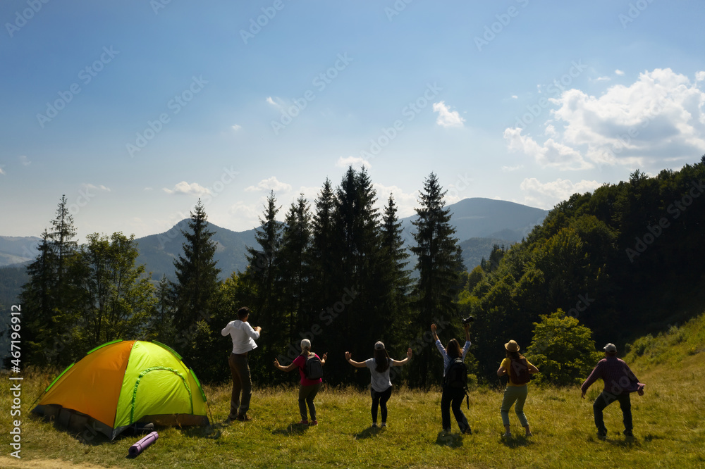 Wall mural group of happy tourists near camping tent in mountains, back view