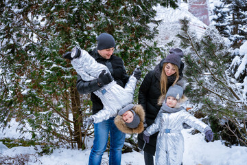 Father and mother hold children in their arms, laughing cheerfully. Family winter walk in forest. Raising child, family habits. Having fun in winter in forest in frosty weather on weekend or holidays